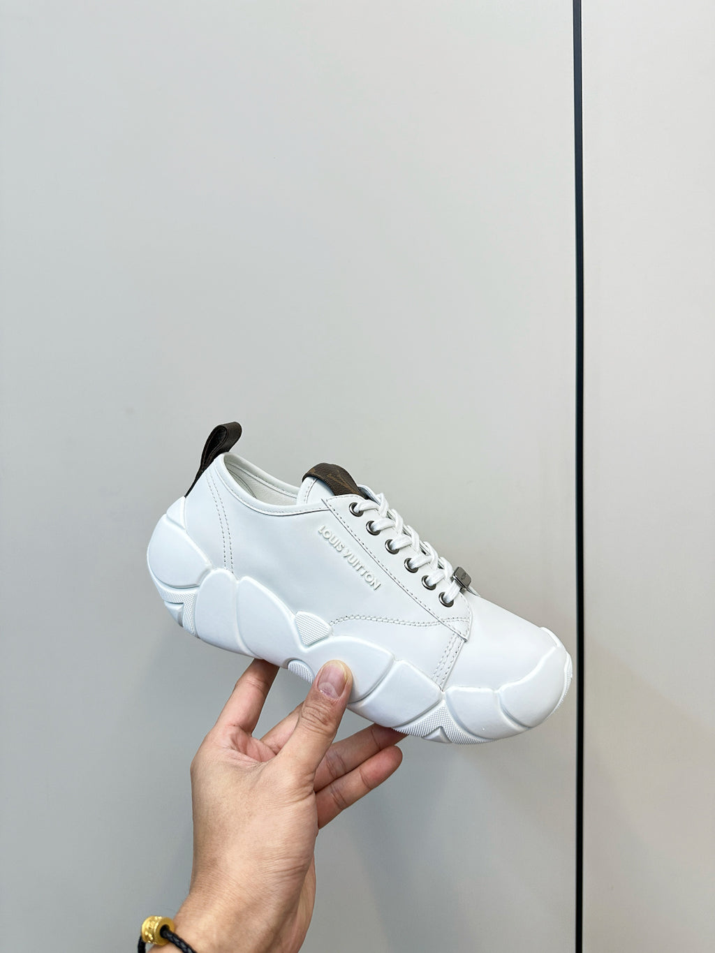 White lace-up sneaker held in hand, showing dark heel detail and chunky sole