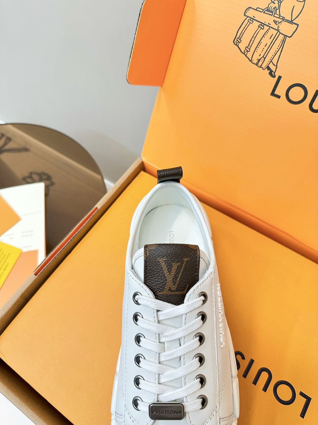 White lace-up sneaker close-up with dark monogram-style heel tab in box