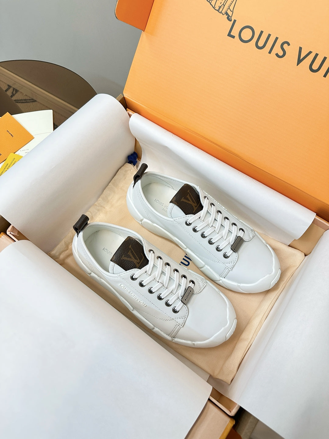 White lace-up sneakers resting in a box, with dark heel tabs and sole details