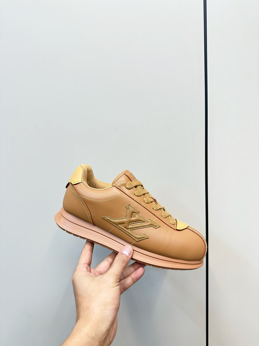 Tan lace-up low-top sneaker held in hand, LV logo on side and front