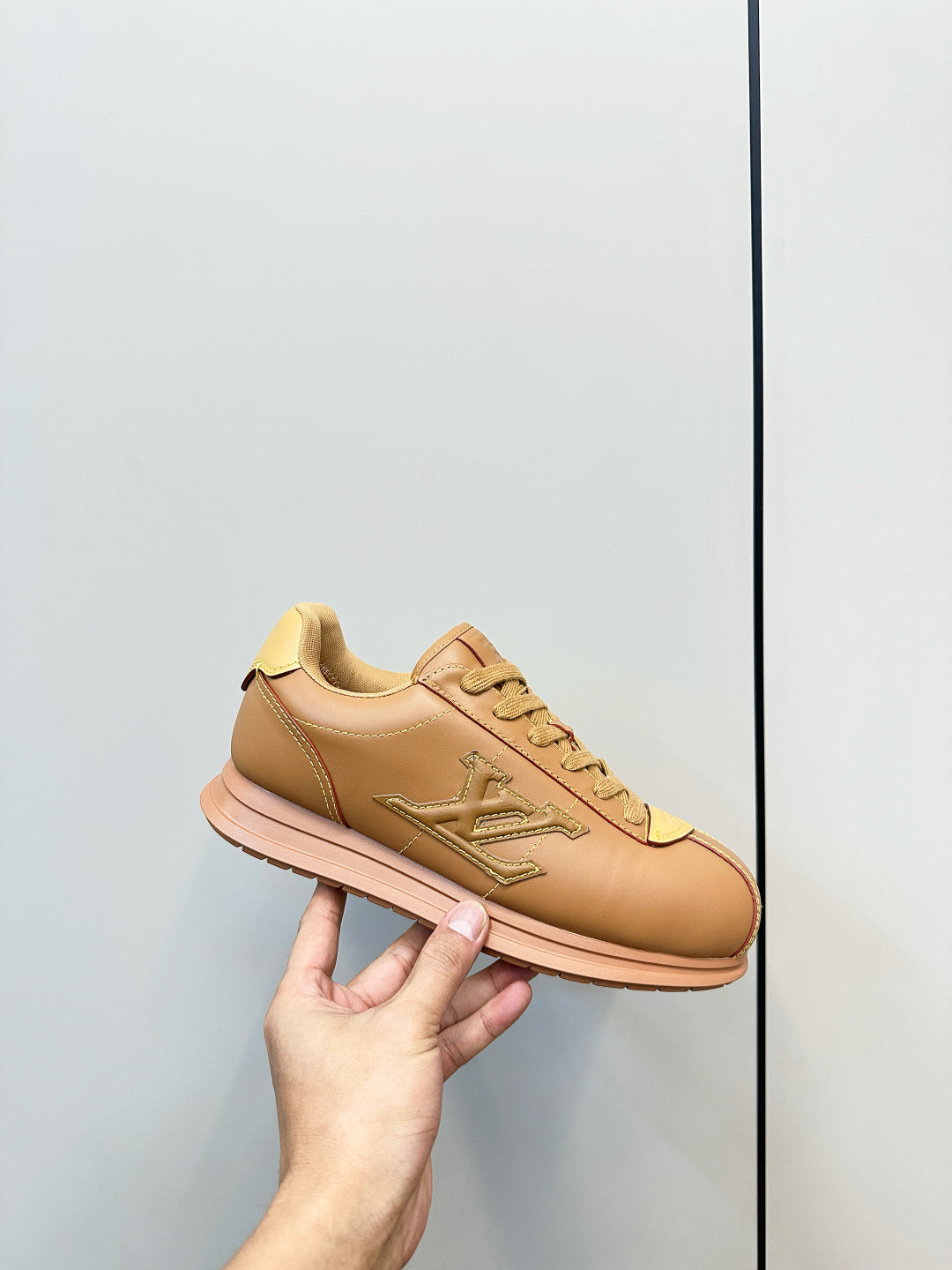 Tan lace-up low-top sneaker held in hand, LV logo on side and front