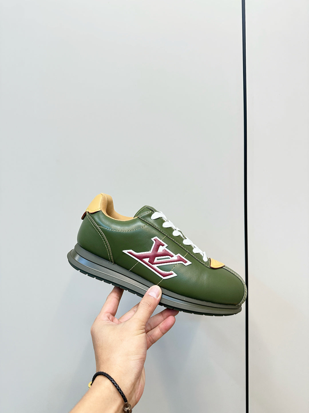 Green low-top sneaker held in hand, white laces and red LV logo