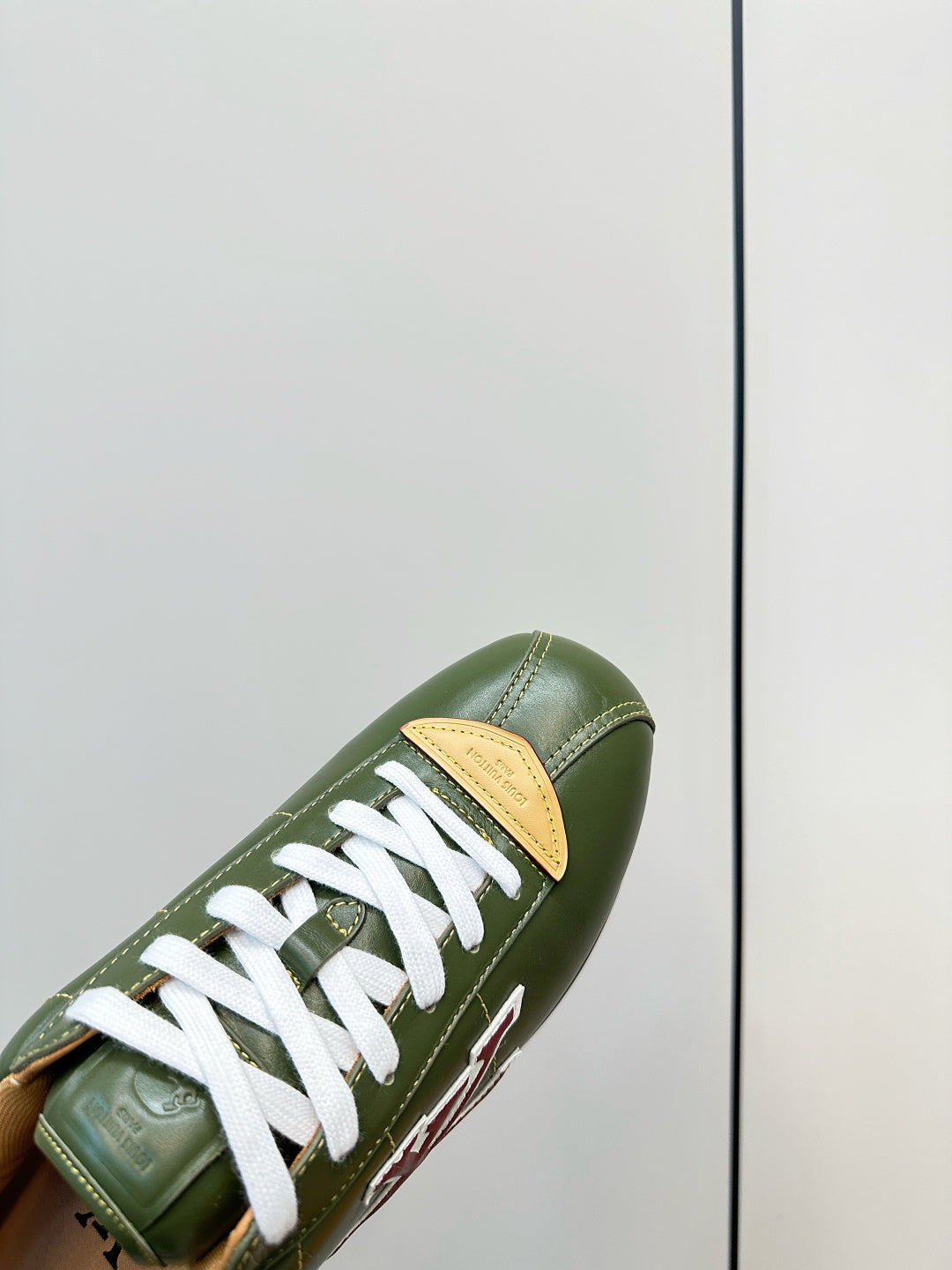 Close-up of green sneaker with white laces and tan panel, side LV mark