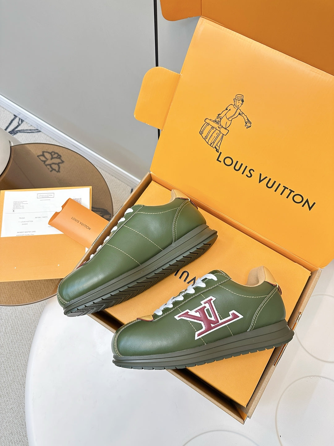 Pair of green low-top sneakers on orange shoebox, white laces and LV logo