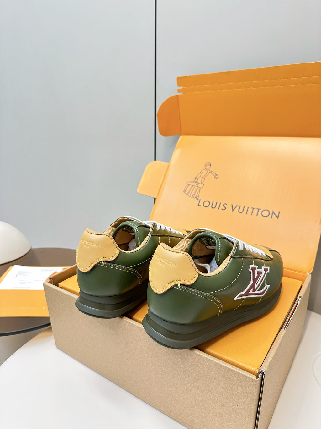 Green low-top sneakers on orange shoebox, white laces and side LV logo