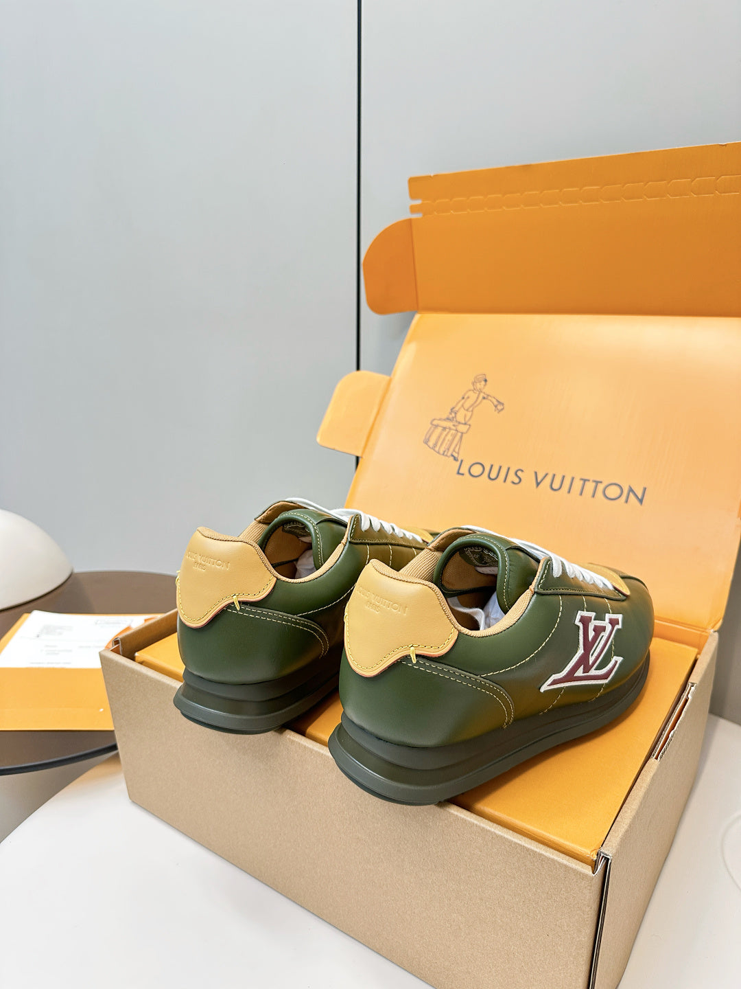 Green low-top sneakers on orange shoebox, white laces and side LV logo
