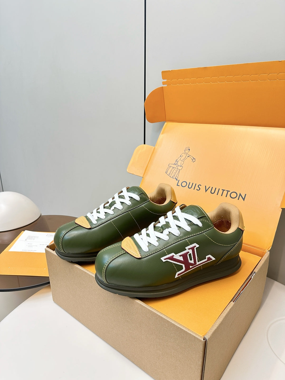 Green low-top sneakers on orange shoebox, white laces and LV logo with red/yellow accents