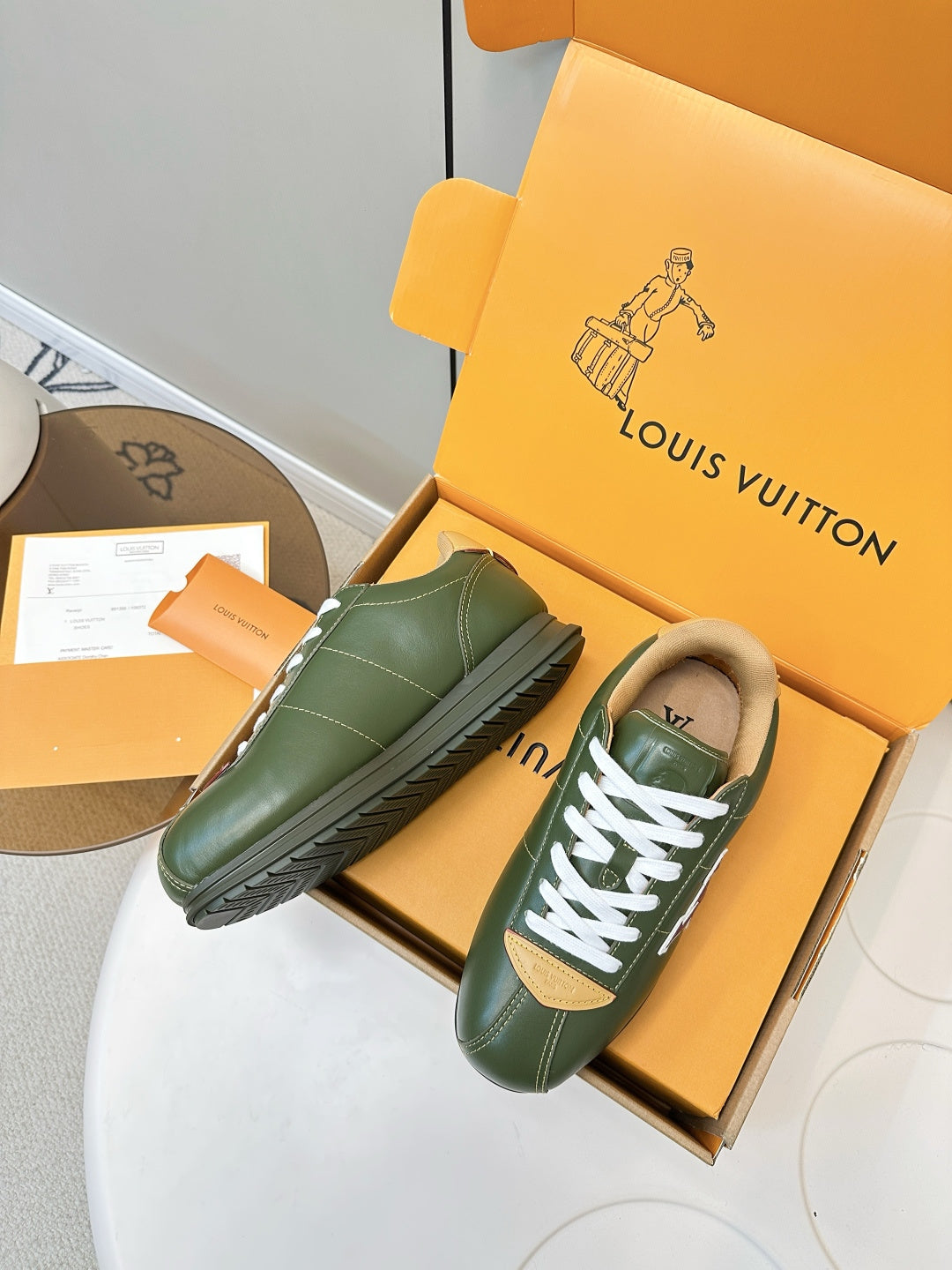 Green leather sneakers with white laces and yellow trim, in open orange box