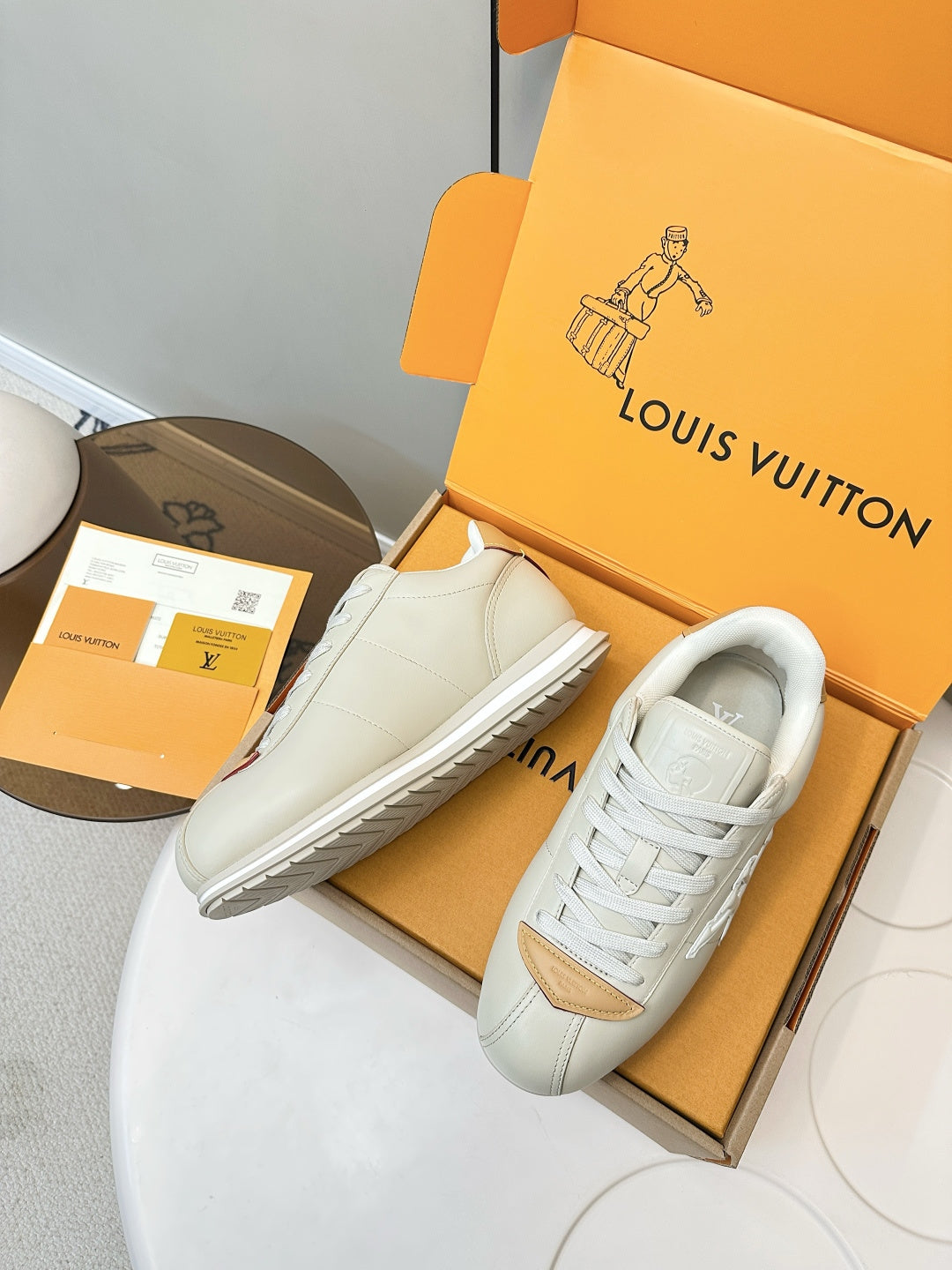 White leather sneakers with tan vamp trim and white laces, shown angled on open box