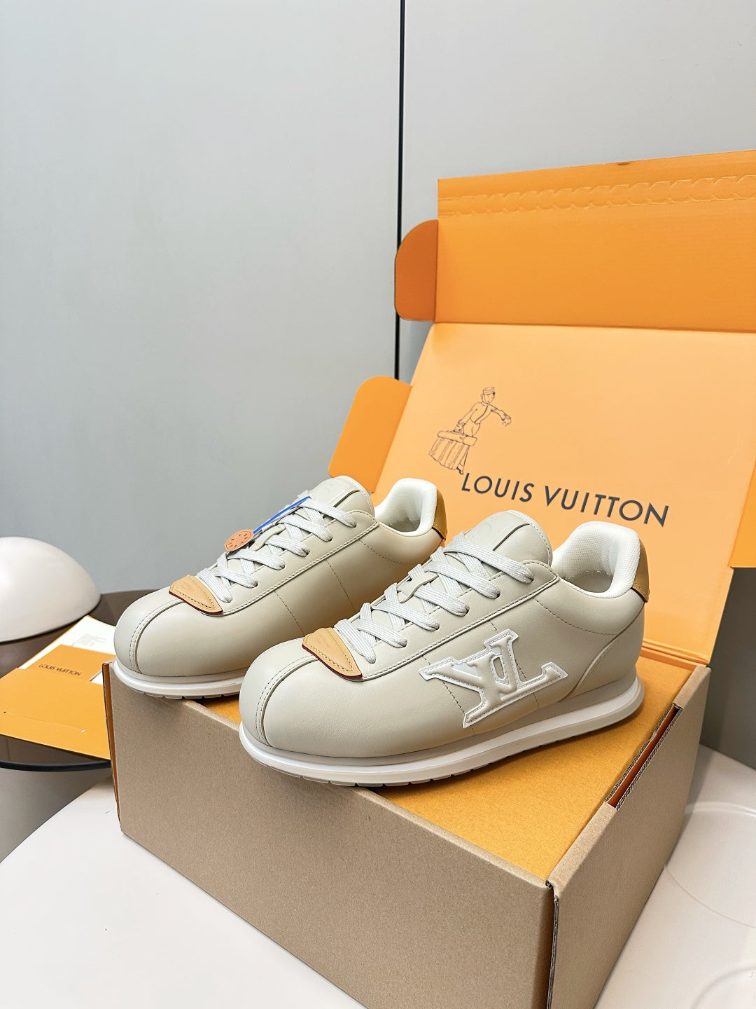 Pair of white leather sneakers with embossed side logo, tan accents, and blue lace strip