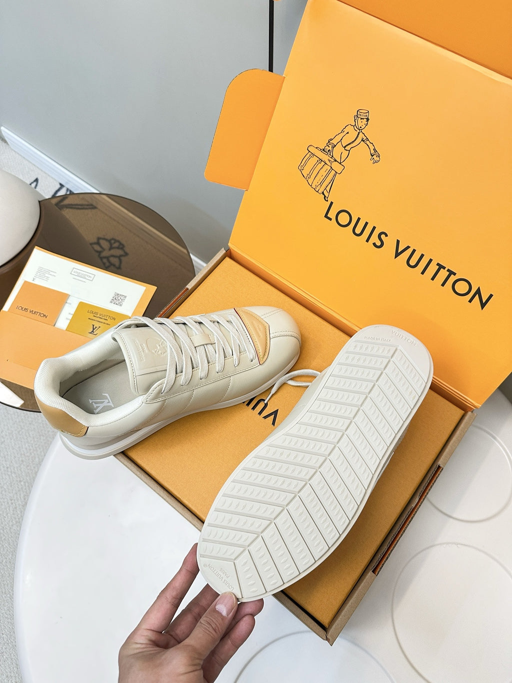 White leather sneakers with textured rubber outsole, tan heel panel, shown from bottom