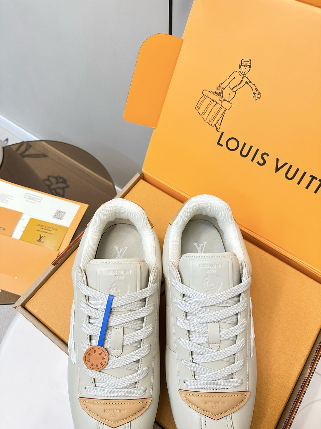 White leather sneakers with tan heel panels and white laces, front view in open box