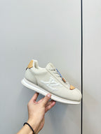 White leather sneaker held in hand, LV-style side logo, tan lace tab and white sole