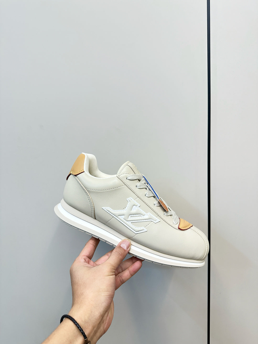 White leather sneaker held in hand, LV-style side logo, tan lace tab and white sole