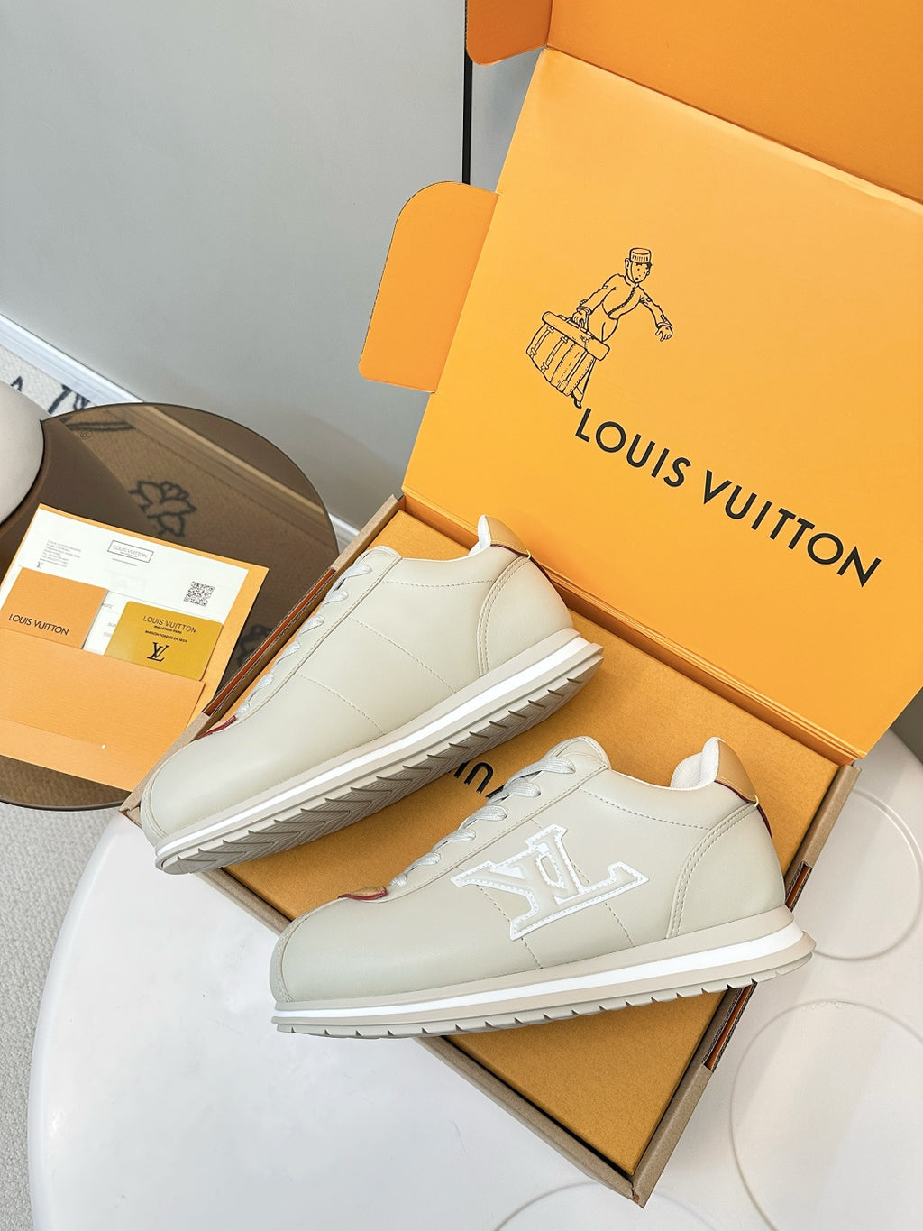 White leather sneakers on box, front pair with tan heel panels and embossed side logo