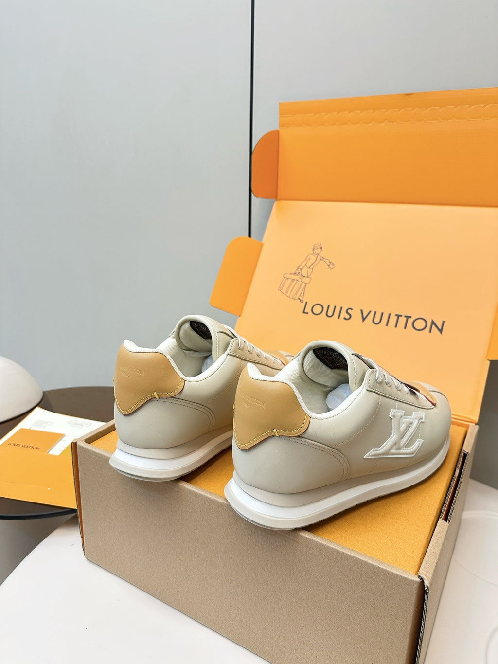 Pair of white leather sneakers with tan heel patches and white rubber sole, angled view