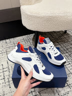 Unisex white sneakers with navy overlays and red collar accents, shown with hand on box