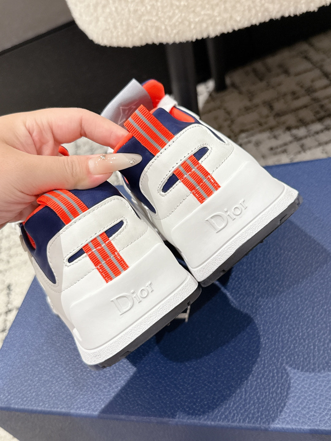 Back view detail of unisex sneakers: white heel with orange-red trim, Dior lettering