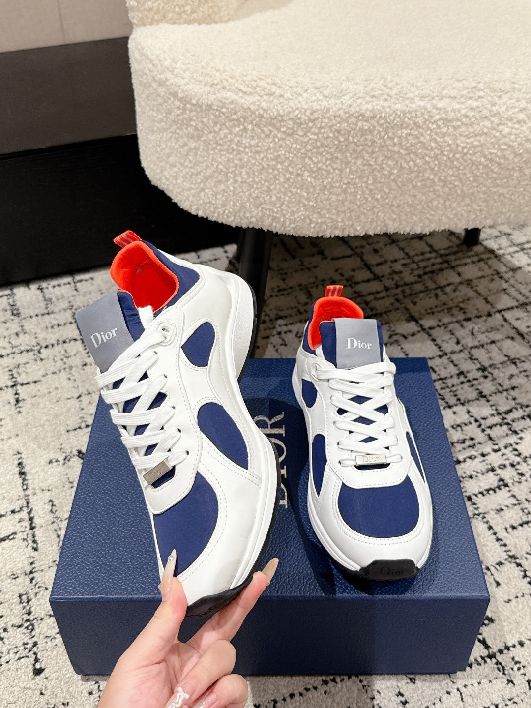 White and navy unisex sneakers with red lining, white laces, hand holding shoe on box
