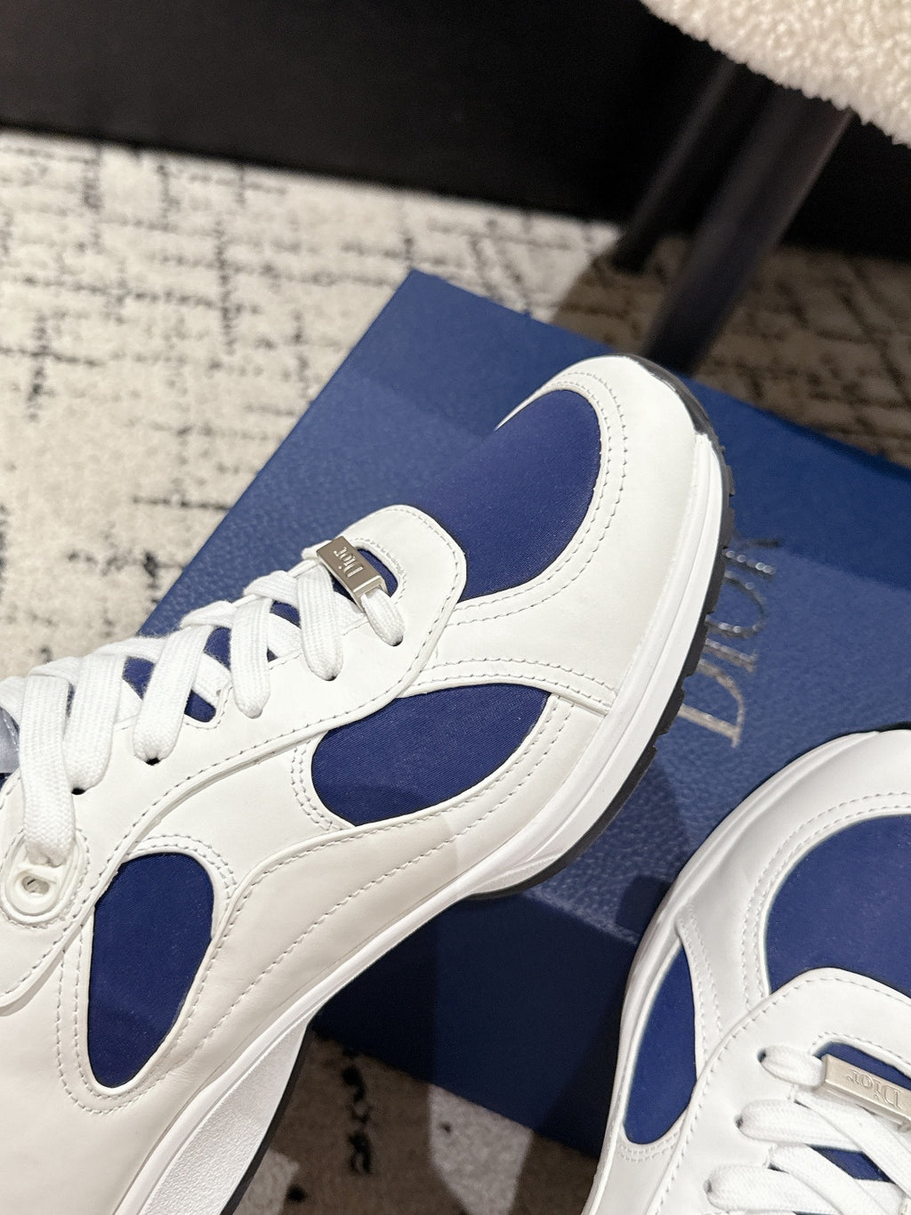 Detail of unisex sneaker side: white leather with navy swoosh-like panel and Dior tab
