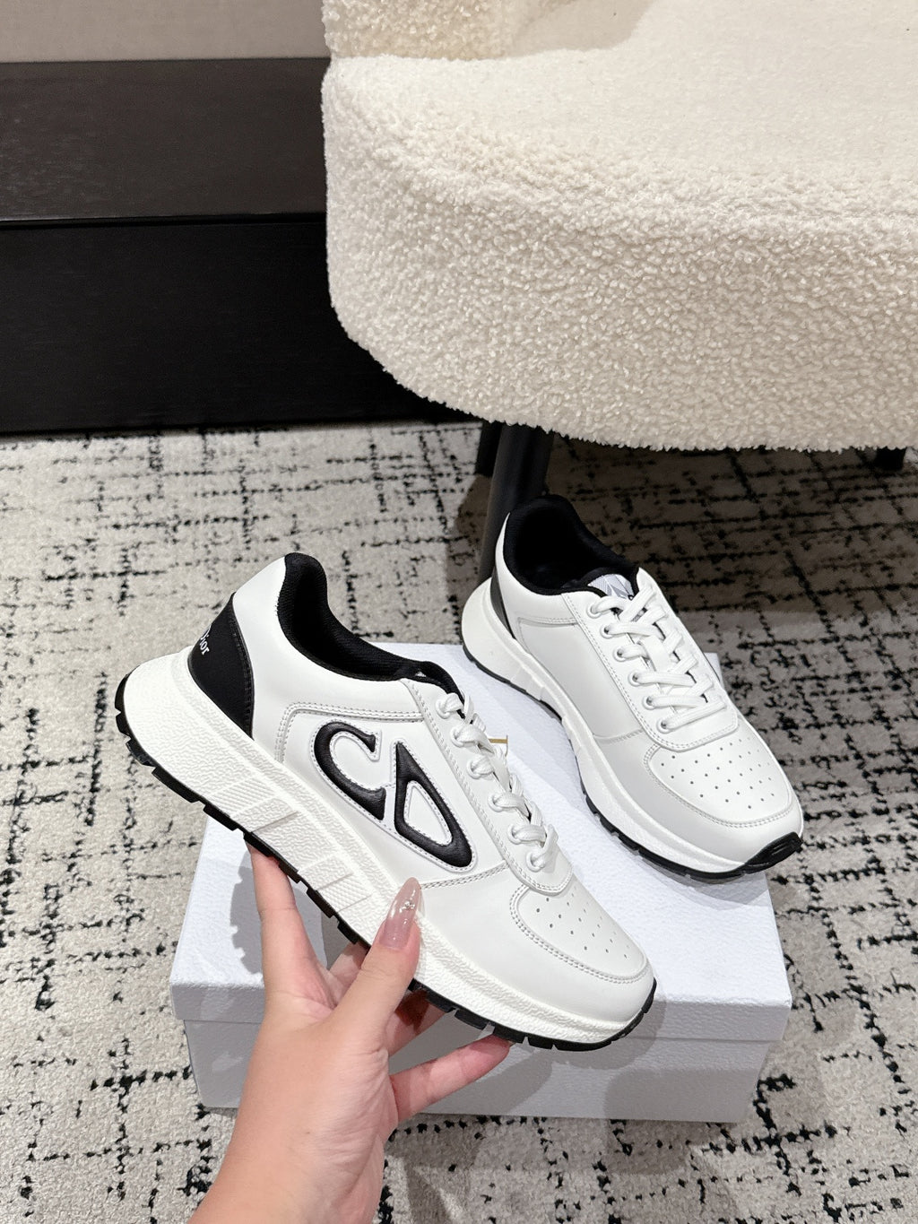 White low-top sneakers with black side panel and 'CD' logo on the box