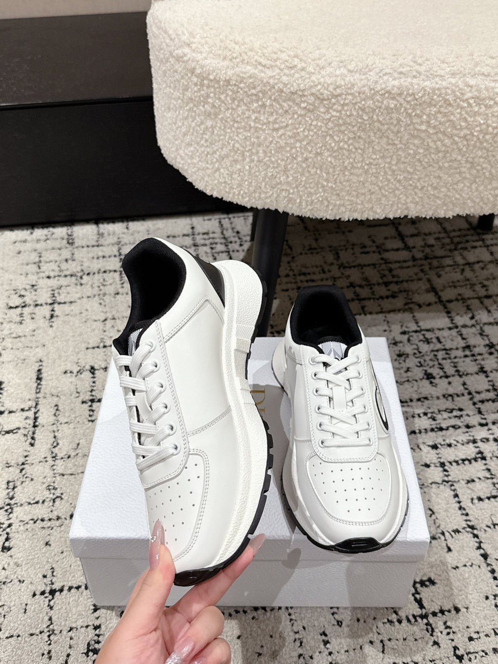 White lace-up sneakers with black collar trim and side logo; hand holding