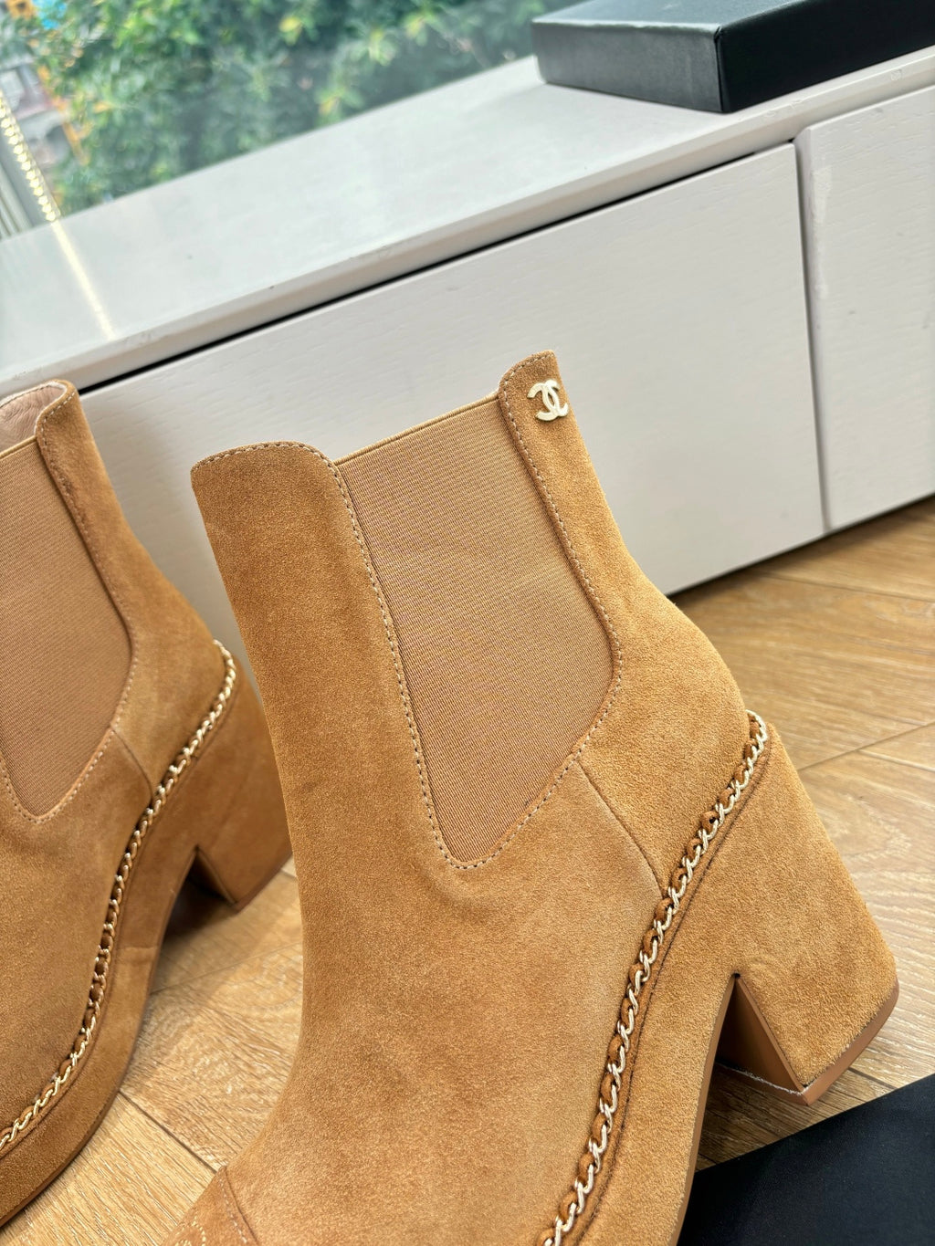 Chanel suede ankle boots close-up: tan upper, chain trim, logo patch on cuff