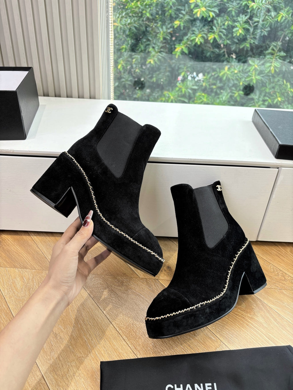 Black suede ankle boots with square heel and chain-stitch trim, held in hand