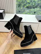 Black suede ankle boots with square heel and chain-stitch trim, held in hand