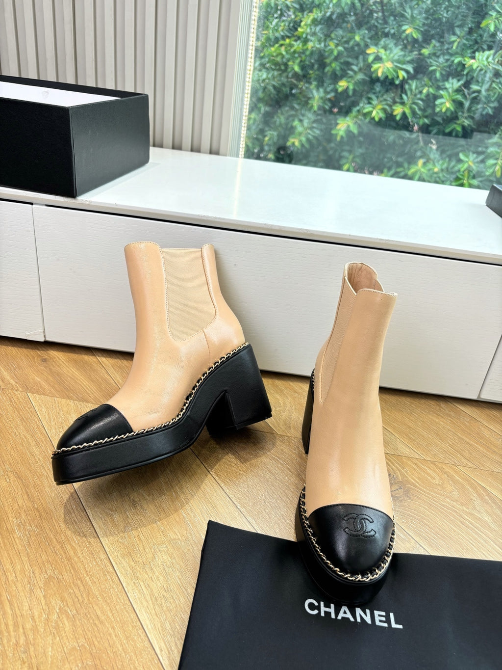 Pair of beige ankle boots with black toe caps, chunky heels, and stitched edges