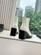White Chelsea boots with black block heel, black side trim, and gold logo medallion