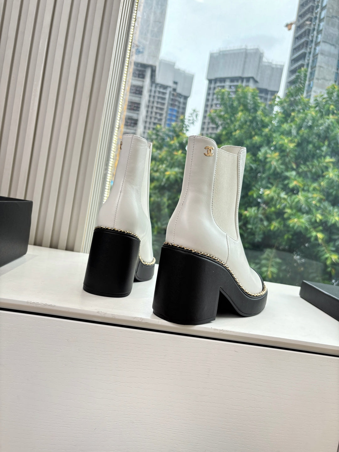 White Chelsea boots with black block heel, black side trim, and gold logo medallion