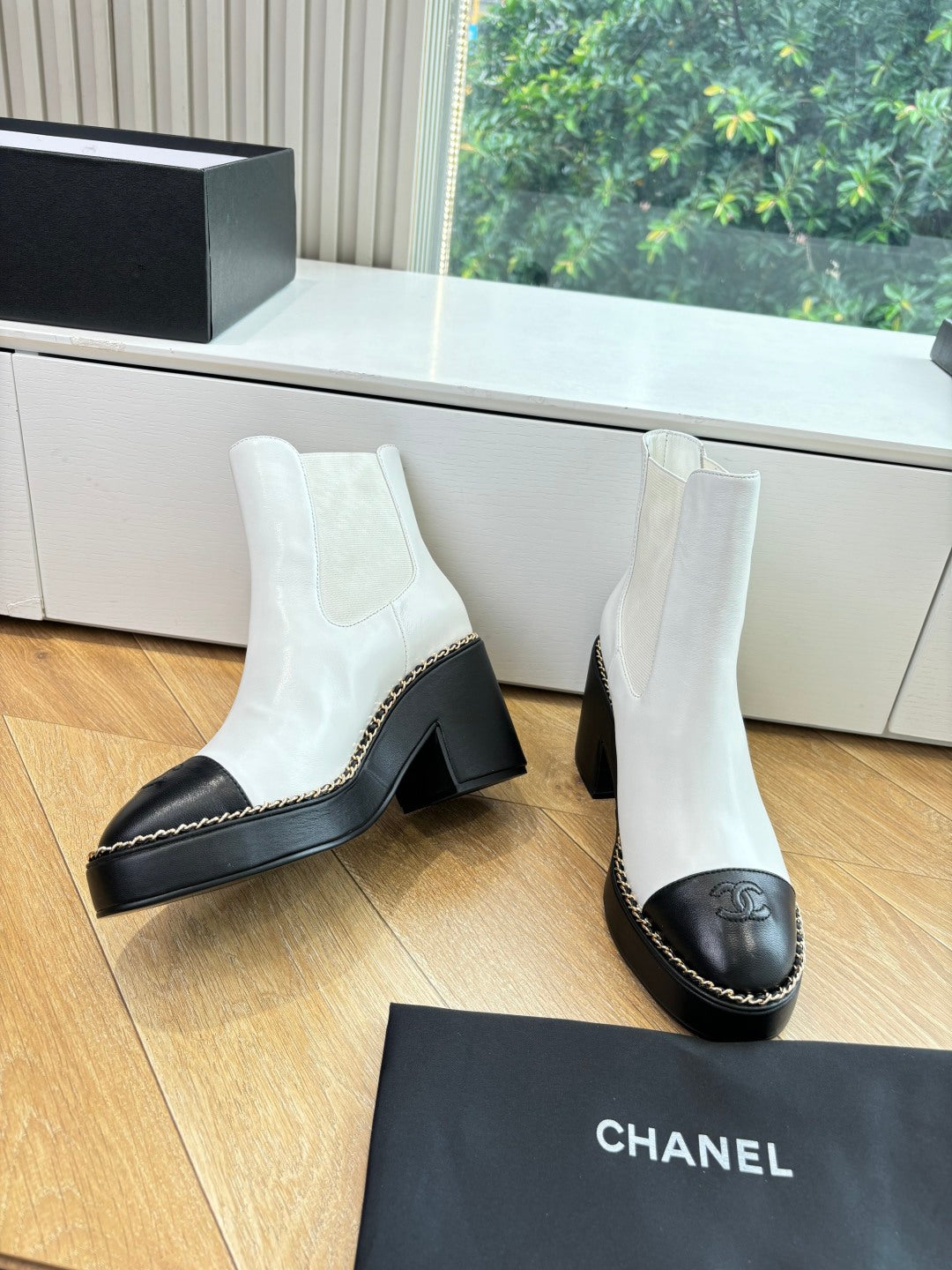 White Chelsea boots with black block heels, gold logo on side, and contrast stitching