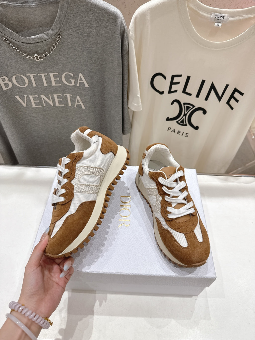 Pair of brown and white sneakers on a display box, hand holding one shoe