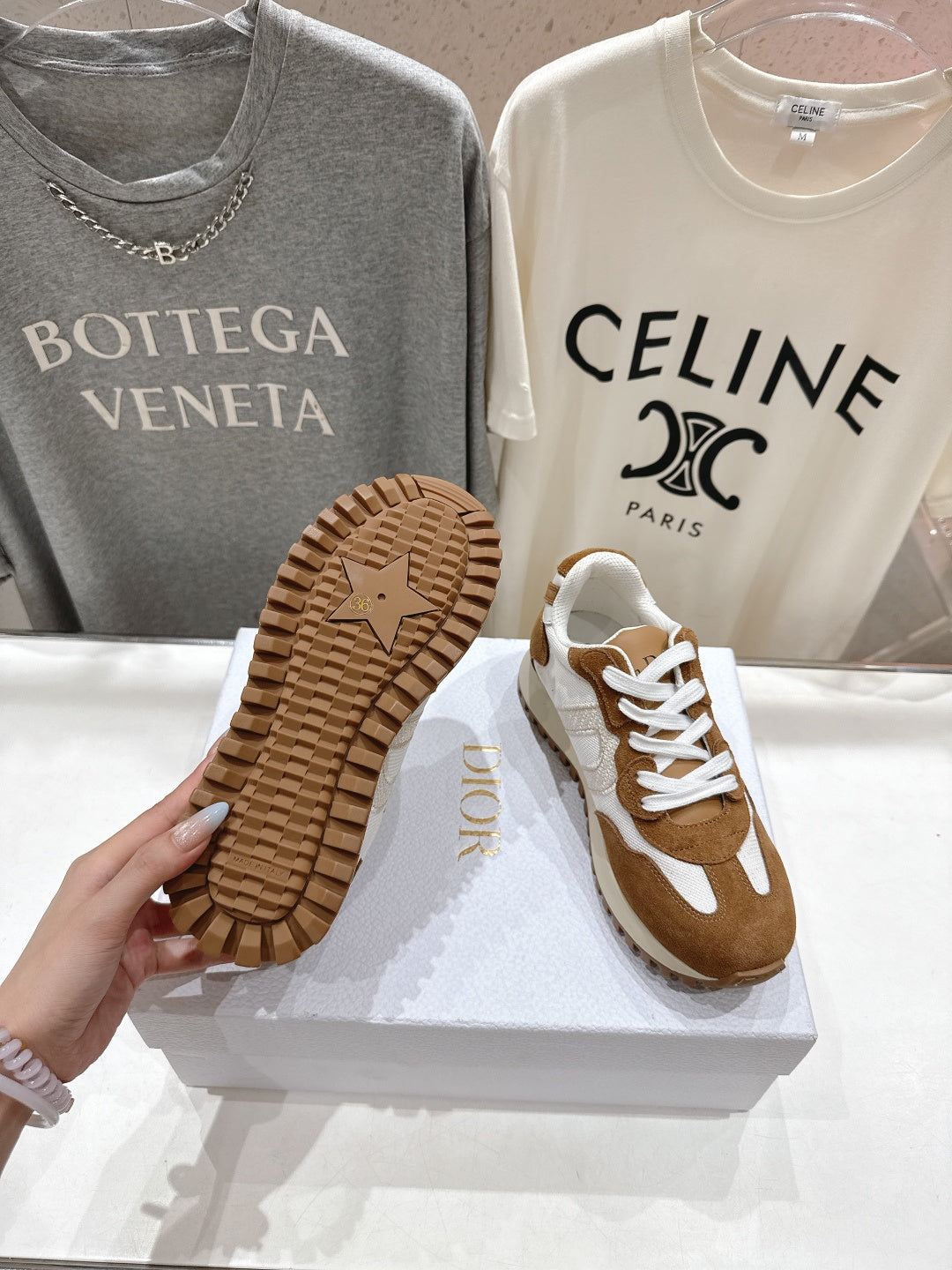 Brown and white sneakers showing outsoles, one shoe angled on display box