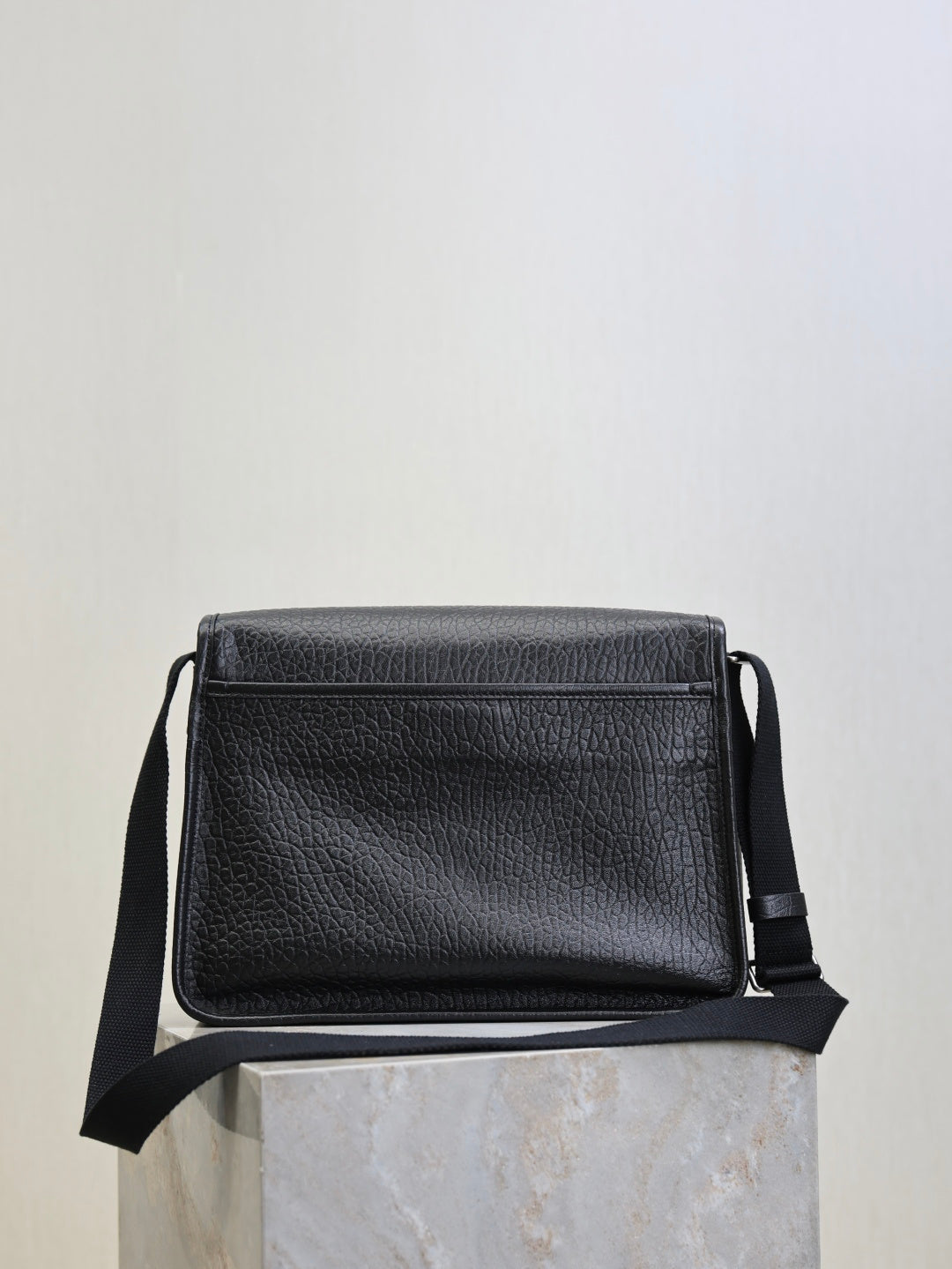 Black textured-leather crossbody bag with front flap and side strap loops