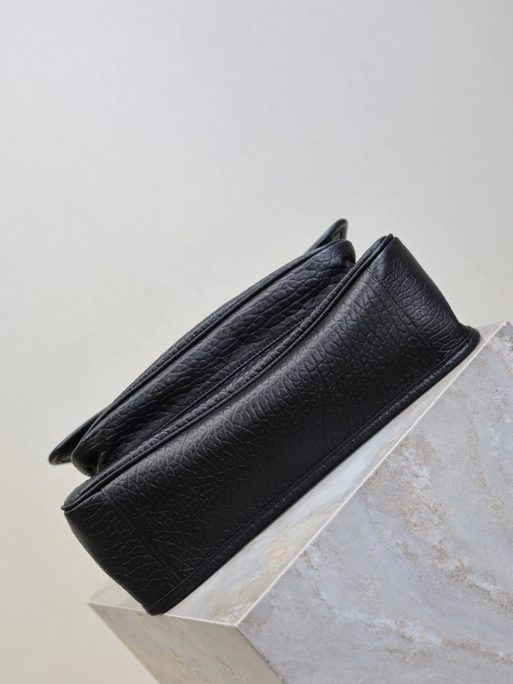 Black textured-leather crossbody bag side view with structured base and seams