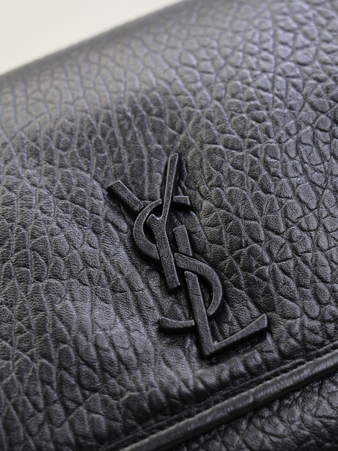 Close-up of black textured-leather flap with YSL logo metal emblem