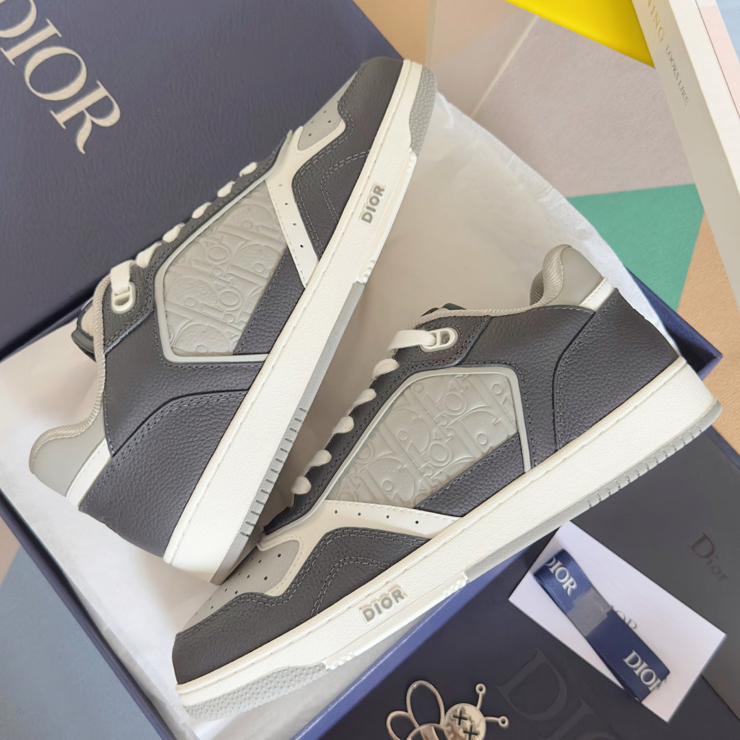 Two low-top Dior sneakers from the side, dark blue leather with white logo strap