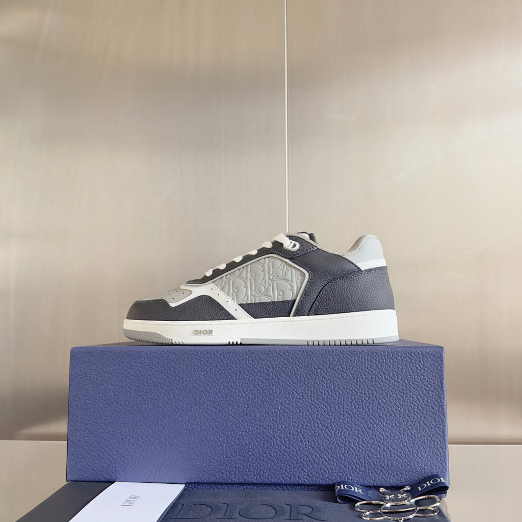 Single low-top Dior sneaker on blue box, dark blue upper with white patterned detail