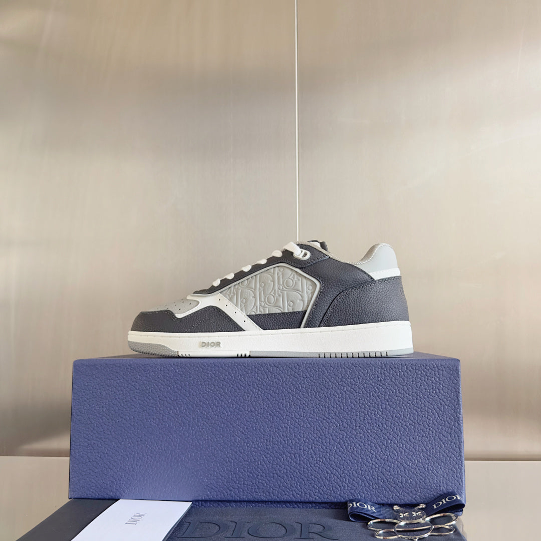 Single low-top Dior sneaker on blue box, dark blue upper with white patterned detail