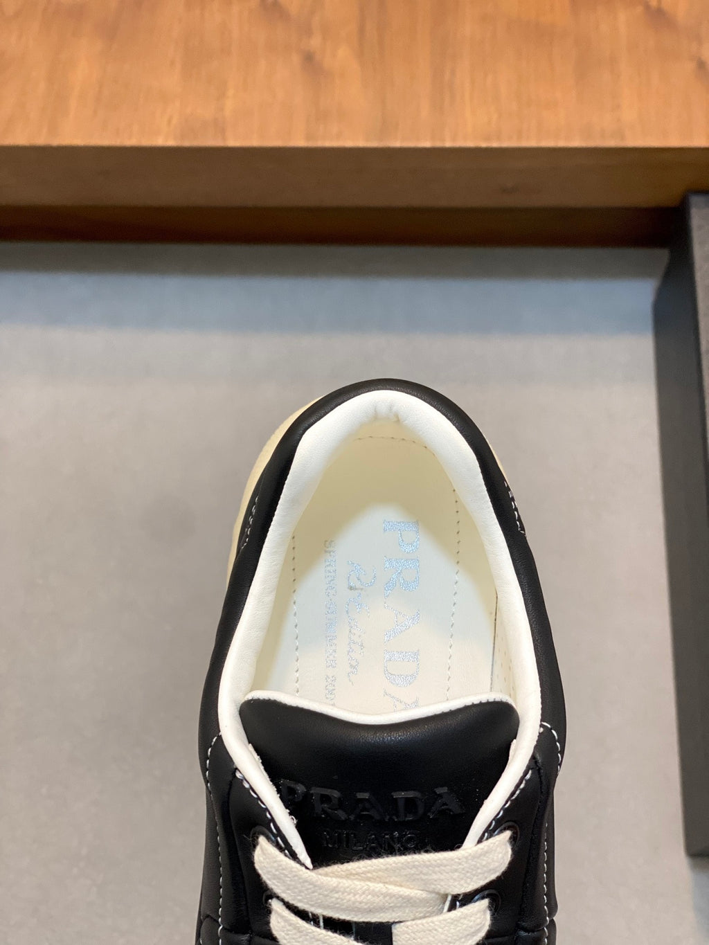 Unisex low-top sneakers with PRADA logo on tongue, black upper and white laces.