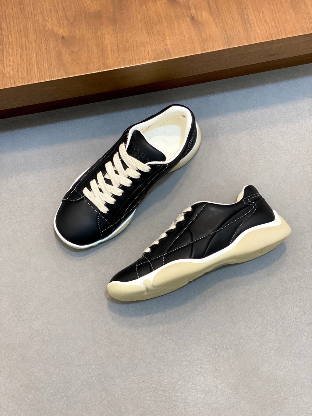 Unisex low-top sneakers pair, black with white laces and cream rubber wedge sole.