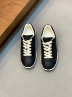 Unisex low-top sneakers, black leather-look with white laces and cream rubber sole.