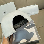 White Balenciaga baseball cap with black strap and logo patch on side.