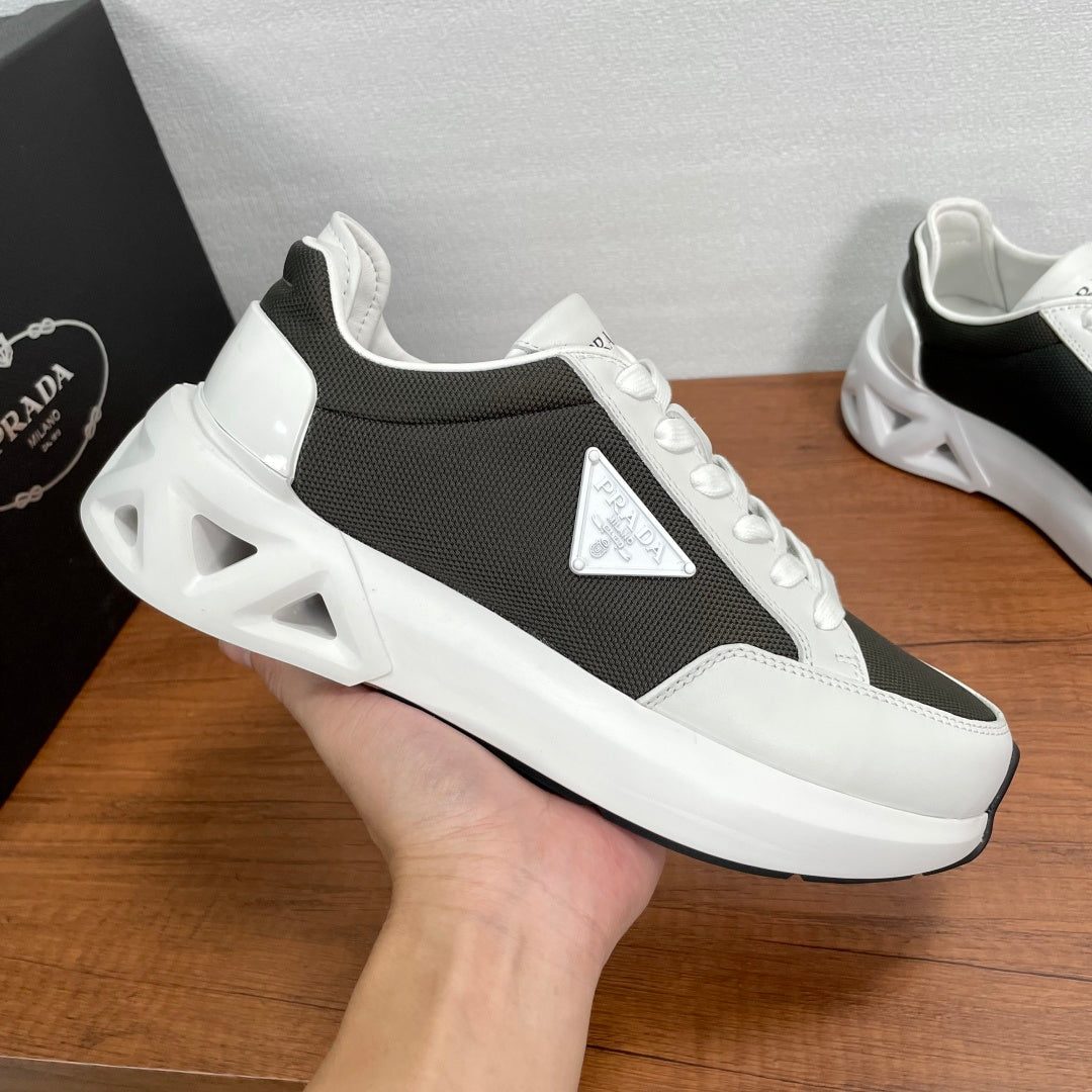 Prada unisex sneaker held up, black and white lace-up with logo patch and chunky sole.