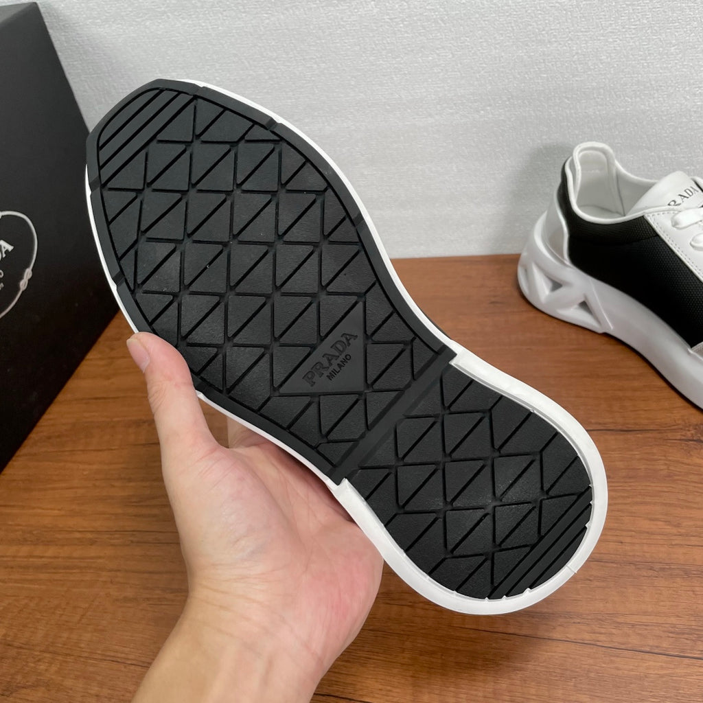 Prada unisex sneaker outsole, black tread with white edge and PRADA logo on sole.