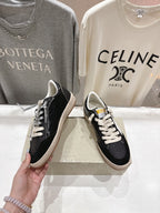 Black low-top sneakers held by hand; white laces and tan rubber sole