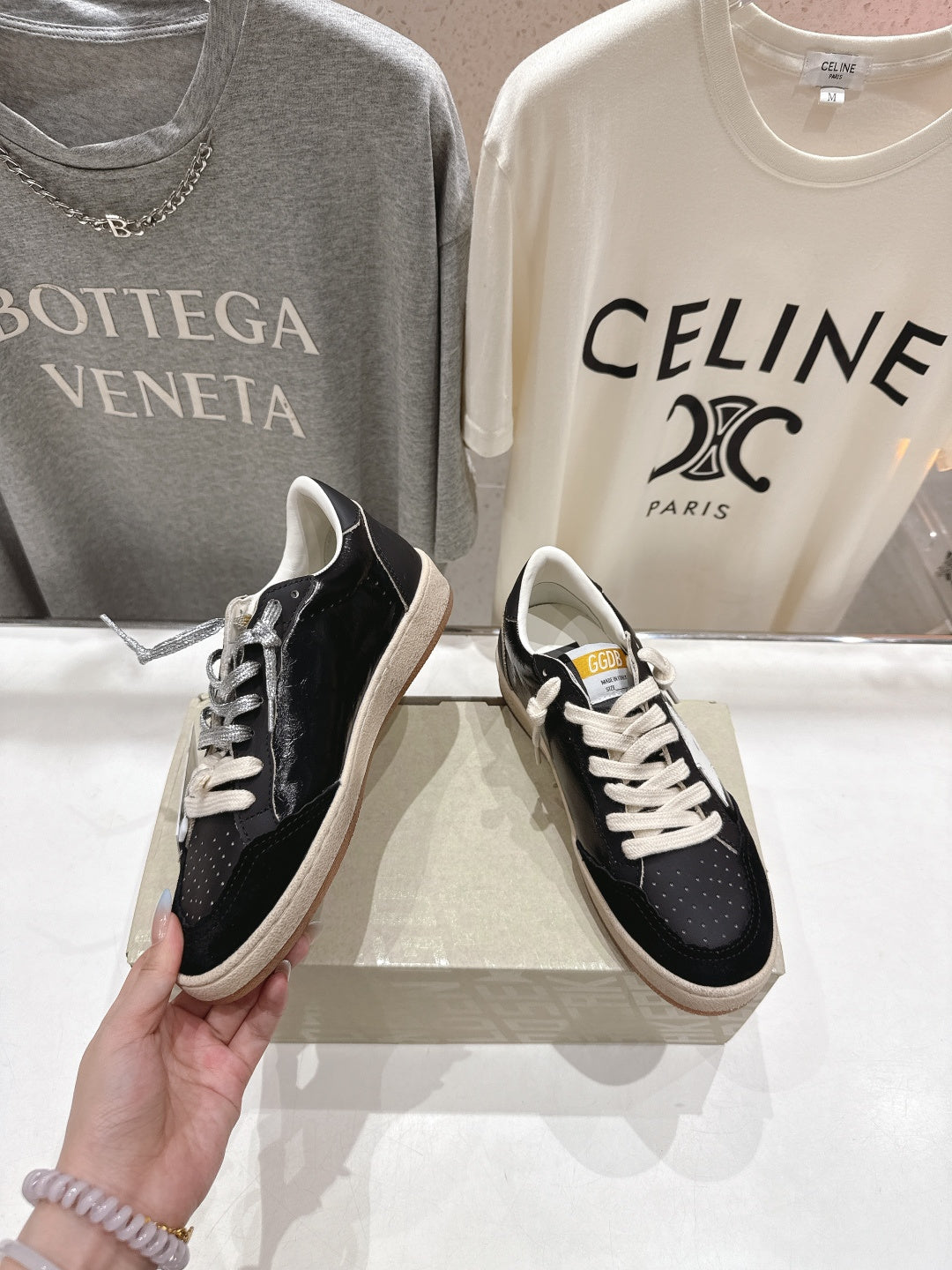 Black low-top sneakers held by hand; white laces and tan rubber sole