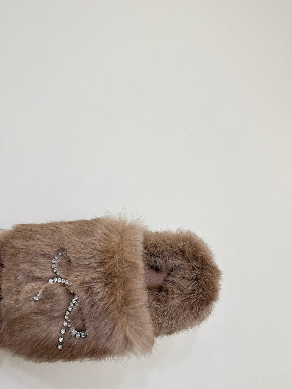Taupe faux-fur slide sandal with rhinestone bow patch on the upper